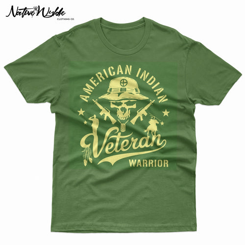 An army green short-sleeve T-shirt with a large graphic print on the front. The graphic features a skull wearing a military boonie hat, crossed rifles, and the words 'AMERICAN INDIAN Veteran WARRIOR' in a bone color.