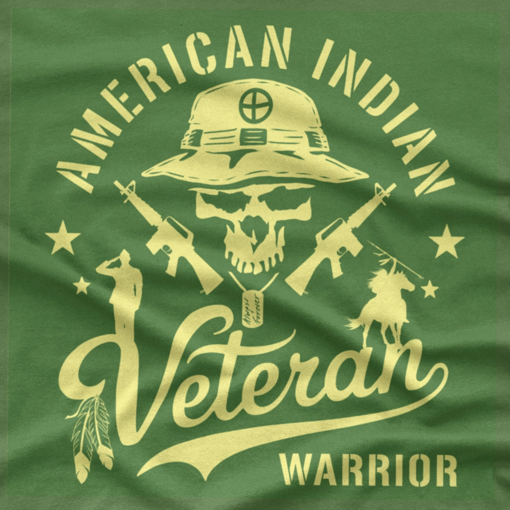 An army green short-sleeve T-shirt with a large graphic print on the front. The graphic features a skull wearing a military boonie hat, crossed rifles, and the words 'AMERICAN INDIAN Veteran WARRIOR' in a bone color.
