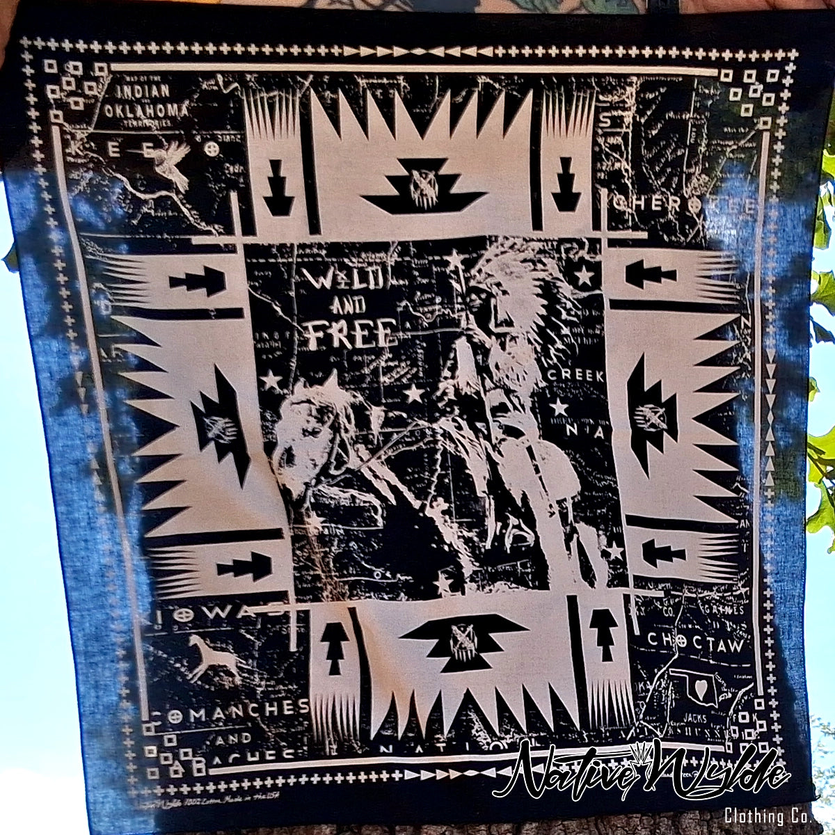A square black and white bandana with a Southwestern geometric pattern, featuring a central graphic of a Native American warrior and text including  'WILD AND FREE'.