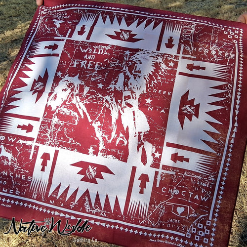 A square bandana laid flat outdoors on grass, featuring a distressed red and white Native American-inspired graphic print with text such as 'Wild and Free,' 'Sierkoe,' and 'Choctaw.' A 'Native Wyld' watermark appears at the bottom left.
