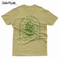 A natural sand-colored T-shirt with a dark green graphic print on the front. The graphic features a central botanical illustration inside an oval, surrounded by the text 'PLANTS ARE NOT ALTERNATIVE MEDICINE', 'INDIGENOUS', and 'THEY ARE THE ORIGINAL'.