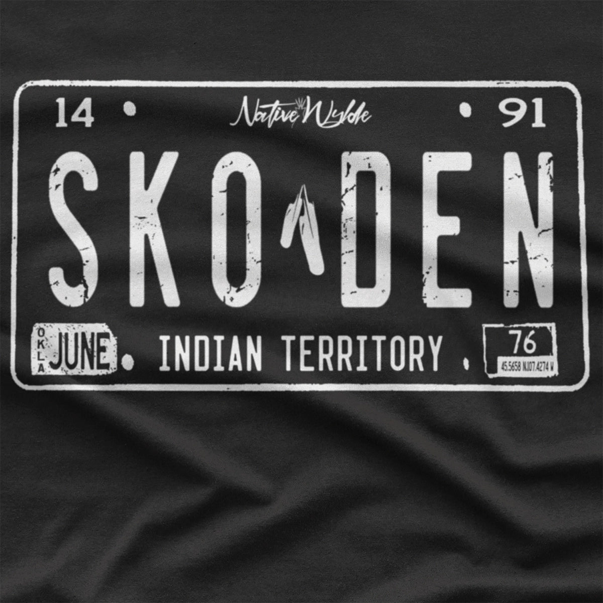 A black short-sleeve t-shirt with a distressed white graphic of a vintage Native American license plate reading 'SKODEN' and 'FROM INDIAN TERRITORY