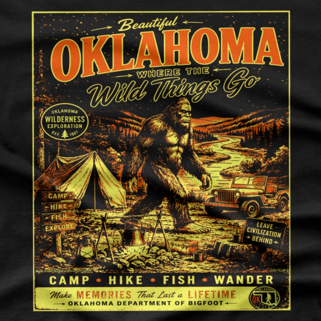 A vintage-style Oklahoma travel poster graphic printed on a black shirt. The design features large orange-red 'OKLAHOMA' lettering, a Bigfoot scene with a tent, jeep, river, and campfire, plus yellow text reading 'Where the Wild Things Go' and 'Make Memories That Last a Lifetime'.