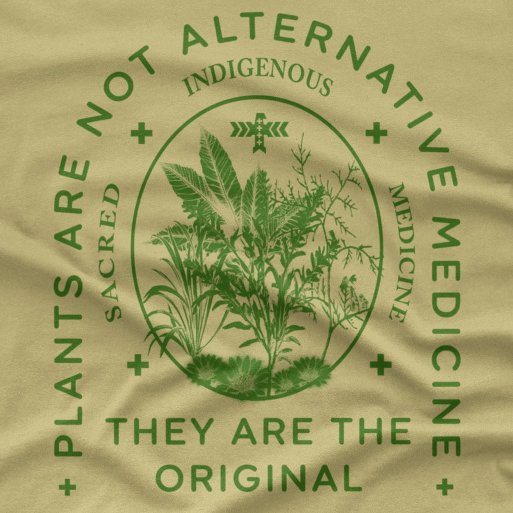 A natural sand-colored T-shirt with a dark green graphic print on the front. The graphic features a central botanical illustration inside an oval, surrounded by the text 'PLANTS ARE NOT ALTERNATIVE MEDICINE', 'INDIGENOUS', and 'THEY ARE THE ORIGINAL'.