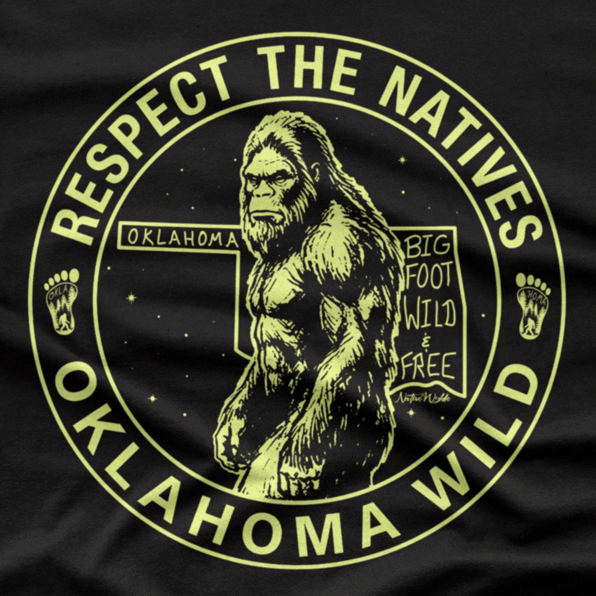 A black short-sleeve crewneck t-shirt featuring a circular graphic print of Bigfoot in the center with the text 'RESPECT THE NATIVES' and 'OKLAHOMA WILD' in bone color around the border. 