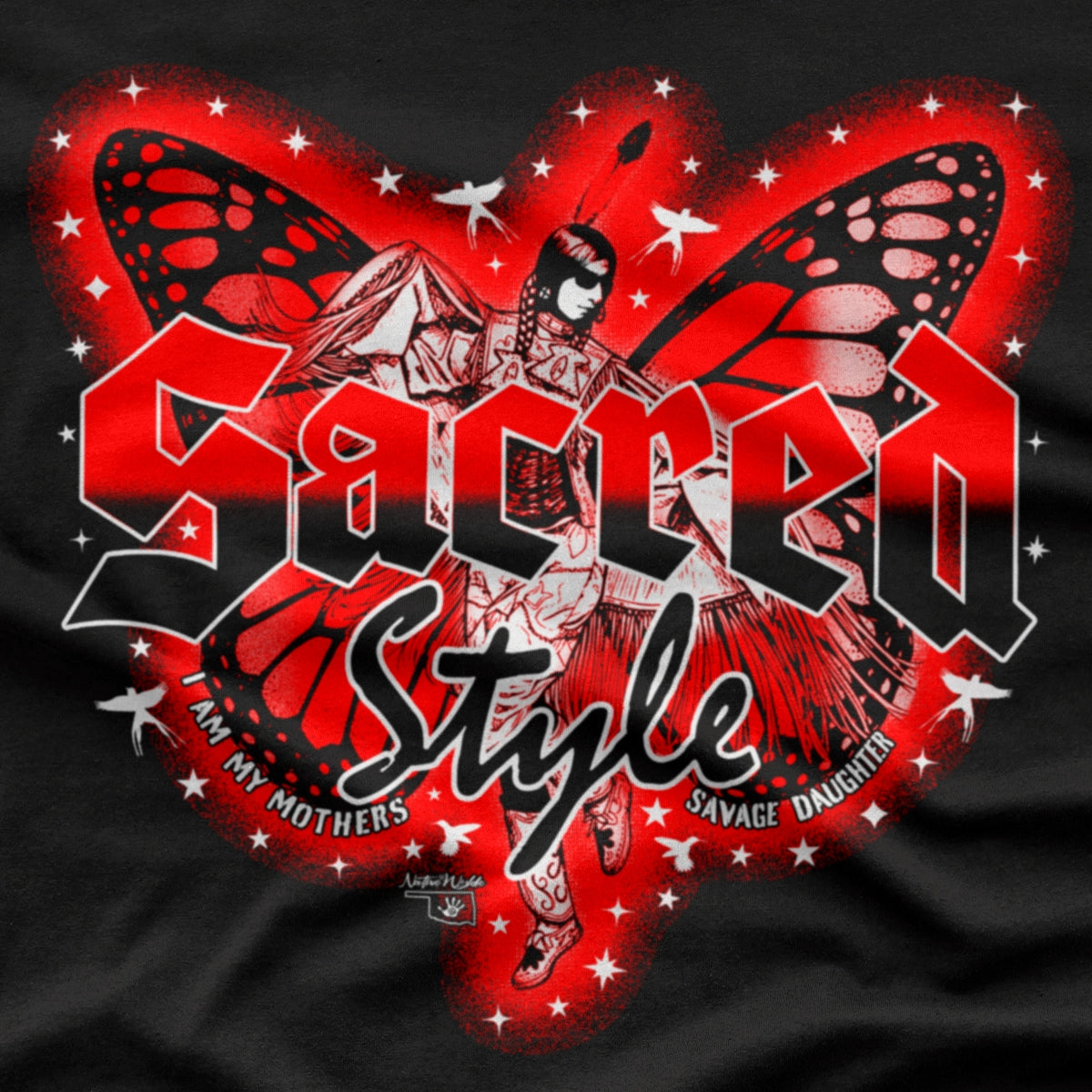 A close-up of a black graphic t-shirt featuring a red and black butterfly design with the text 'Sacred Style' and 'I AM MY MOTHERS SAVAGE DAUGHTER'. Fancy shawl Native American dancer in the middle of the wings.