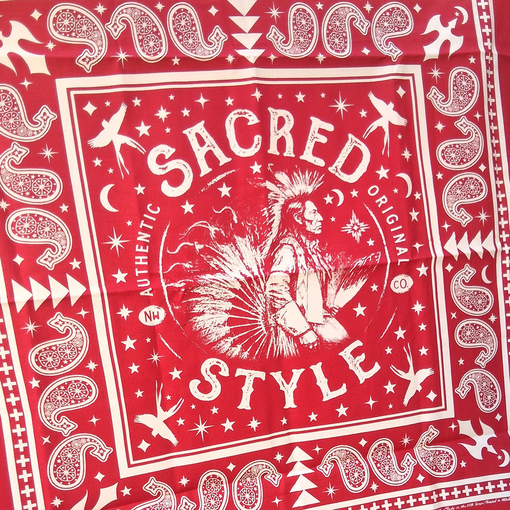 A red bandana featuring a white graphic print with the words 'SACRED STYLE' and a central Native American profile illustration, surrounded by stars, moons, and geometric border patterns.