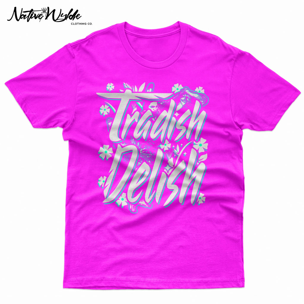 A bright pink crewneck t-shirt featuring a large graphic on the front that reads 'Tradish Delish' in stylized white and light blue lettering with small floral accents and a Native American Shawl Dancer.